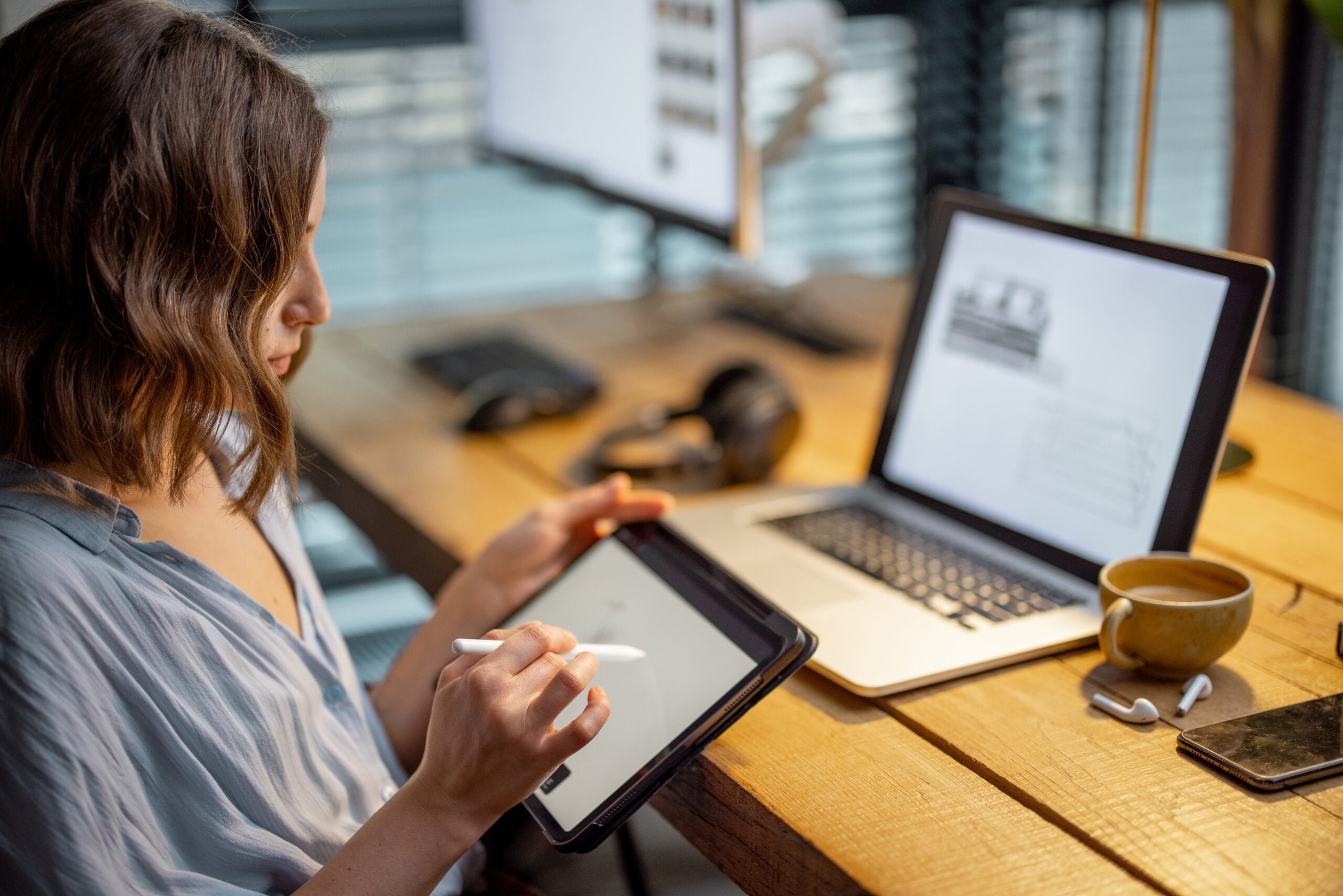 Young woman dressed casually having some creative work, drawing on a digital tablet, sitting at the cozy and stylish home office